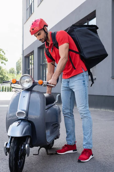 Corriere arabo con zaino termo in piedi vicino scooter all'aperto — Foto stock