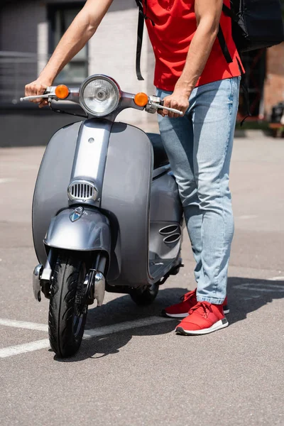 Vista recortada de mensajero con mochila térmica de pie cerca de scooter al aire libre - foto de stock