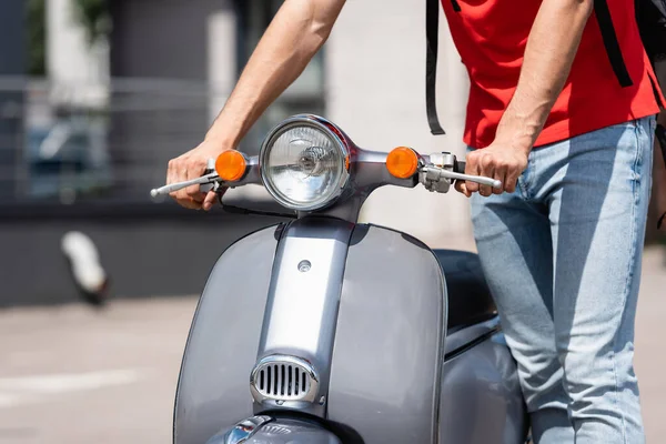 Vista cortada de entregador de pé perto de scooter ao ar livre — Stock Photo