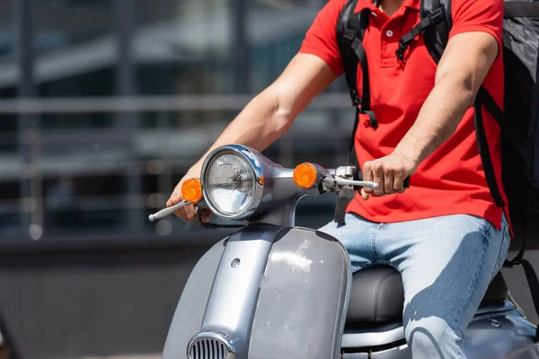 Cropped view of courier with backpack driving scooter outdoors — Stock Photo