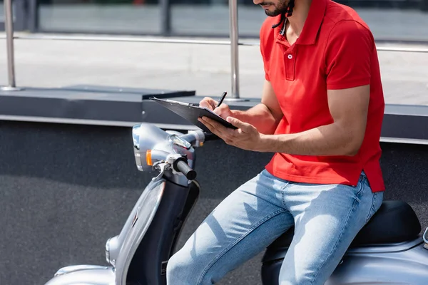 Ausgeschnittene Ansicht des Kurierschreibens auf Klemmbrett auf dem Roller auf der städtischen Straße — Stockfoto