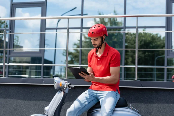 Arabischer Kurier in rotem T-Shirt und Helmaufschrift auf Klemmbrett auf Roller im Freien — Stockfoto