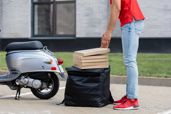 Vista recortada del mensajero poniendo cajas de pizza en la mochila termo cerca de scooter al aire libre - foto de stock