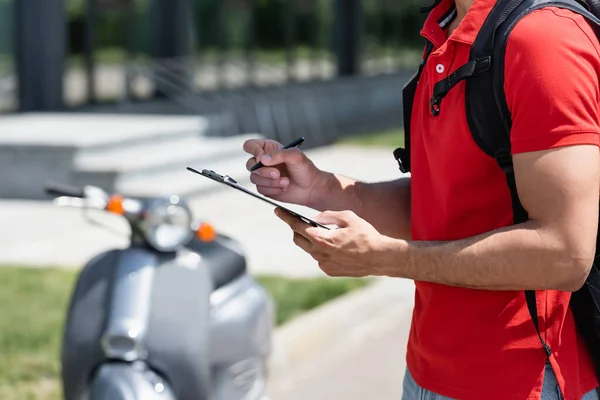 Vista ritagliata della penna di tenuta del corriere e degli appunti vicino allo scooter sfocato — Foto stock