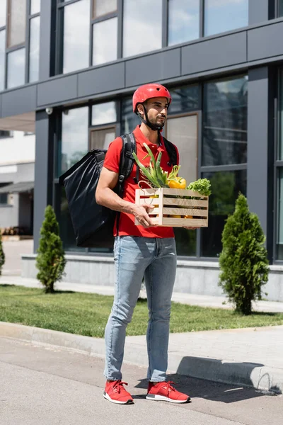 Courier arabe dans un casque de protection tenant boîte avec des légumes en plein air — Photo de stock