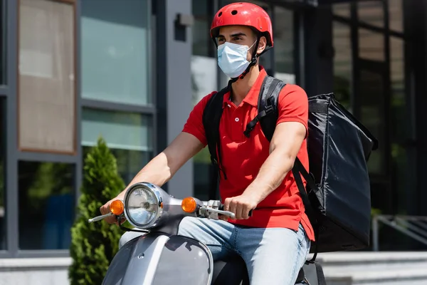Courrier musulman en masque médical avec sac à dos thermique scooter d'équitation à l'extérieur — Photo de stock