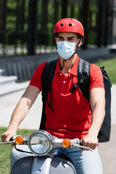 Arabian deliveryman in protective mask riding scooter outdoors — Stock Photo