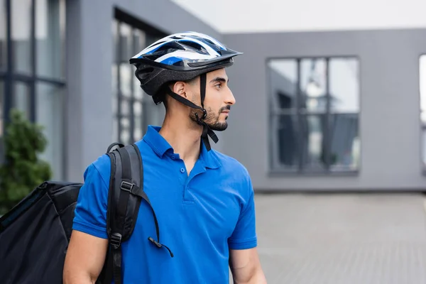 Side view of arabian courier in protective helmet with backpack outdoors — Stock Photo