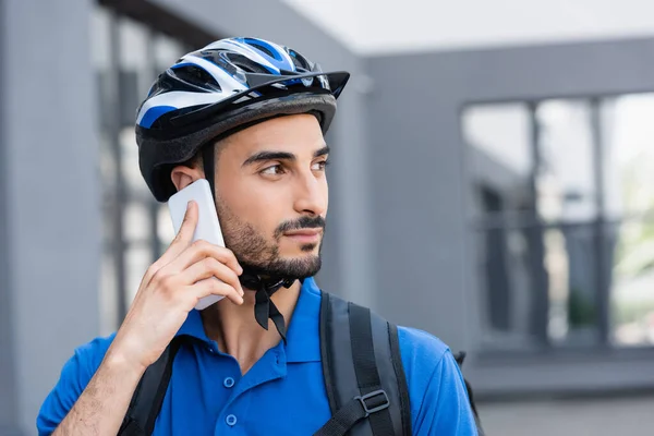 Мусульманский курьер в защитном шлеме разговаривает по мобильному телефону на улице — стоковое фото