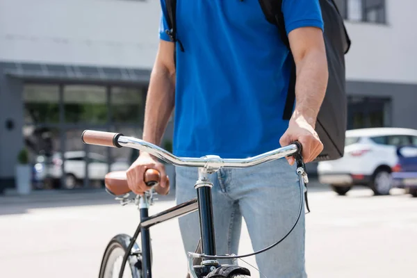 Cropped view of courier with thermo backpack standing near bicycle outdoors — Stock Photo