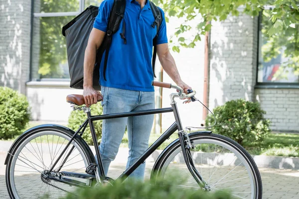 Cropped view of courier with thermo backpack walking near bicycle outdoors — Stock Photo