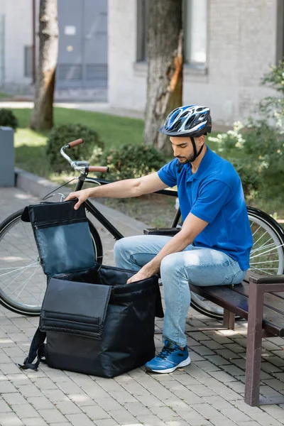 Young muslim courier opening thermo backpack near bike outdoors — Stock Photo