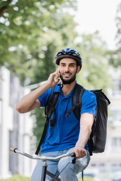 Joven repartidor musulmán con mochila hablando en smartphone - foto de stock