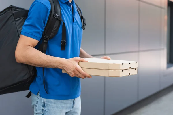 Vista ritagliata del fattorino con zaino che tiene scatole di pizza vicino all'edificio sfocato all'aperto — Foto stock