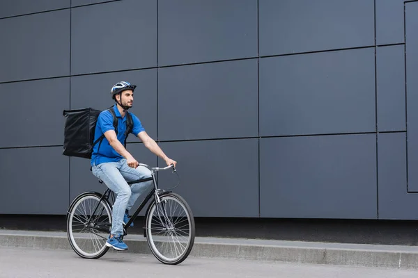 Arabian deliveryman with backpack riding bicycle near building — Stock Photo