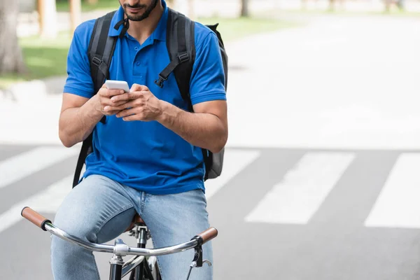 Vista cortada do correio usando o smartphone ao andar de bicicleta ao ar livre — Fotografia de Stock