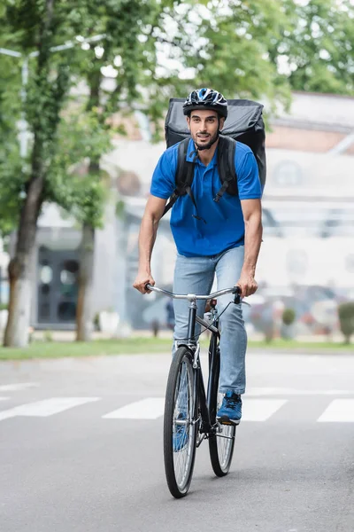 Muslim courier with backpack riding bicycle on urban street — Stock Photo