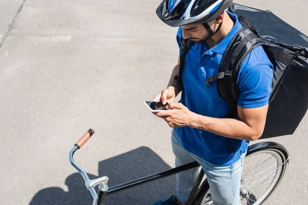 High angle view of arabian deliveryman with backpack using smartphone near bike outdoors — Stock Photo