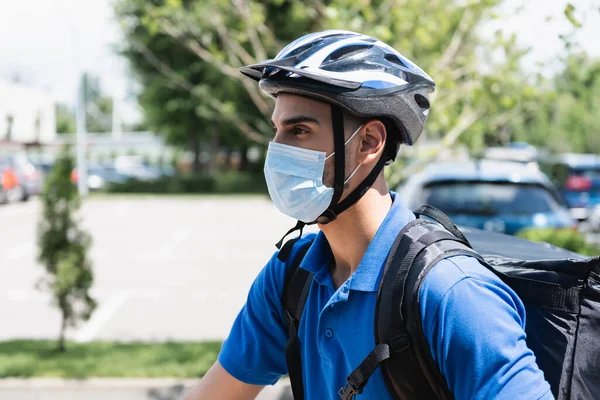 Muslim deliveryman in safety helmet and medical mask outdoors — Stock Photo