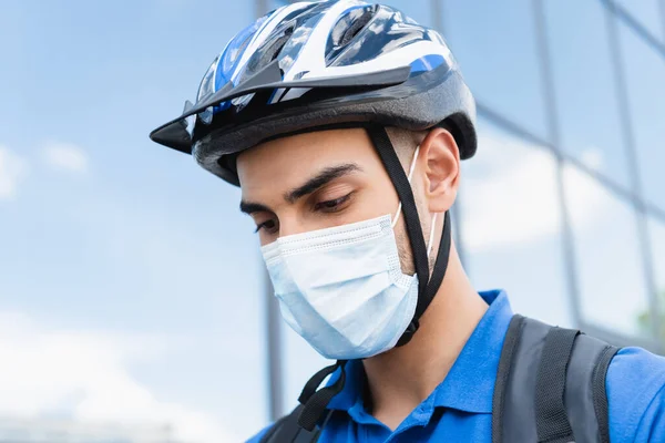 Joven repartidor árabe en casco de bicicleta y máscara médica al aire libre - foto de stock