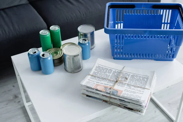 Vista de alto ángulo de periódicos, latas de lata y cesta en la mesa - foto de stock