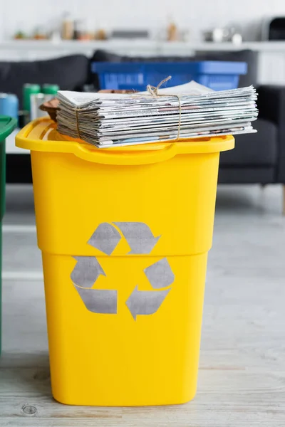 Jornais em lata de lixo com sinal de reciclagem em casa — Fotografia de Stock