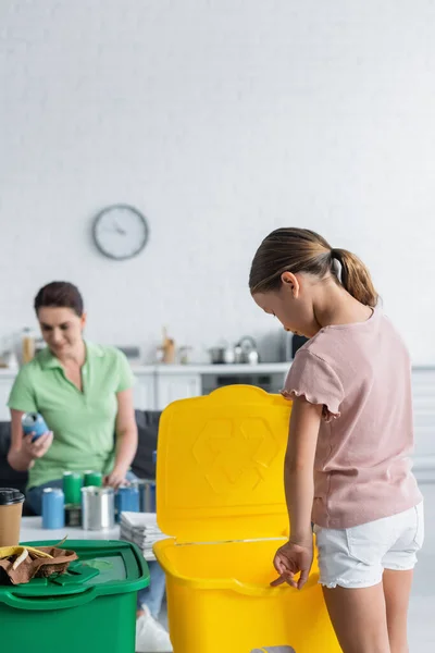 Enfant debout près de la poubelle et mère floue dans la cuisine — Photo de stock