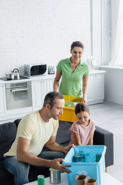 Lächelnde Frau hält Schachtel in der Nähe der Familie und sortiert Müll in Küche — Stockfoto