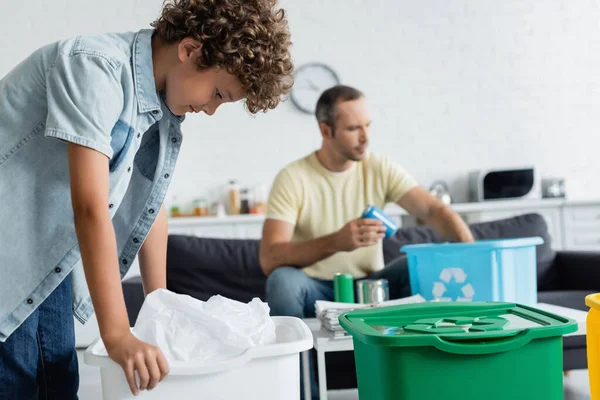 Хлопець, що стоїть біля сміттєзвалища і розмитий батько зі сміттям вдома. — стокове фото