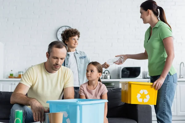 Famiglia e bambini smistamento rifiuti in scatole con segno di riciclaggio in cucina — Foto stock