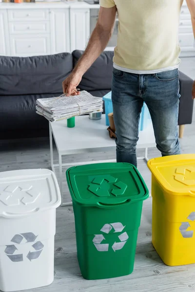 Cropped view of man holding newspapers near trash cans with recycle sign in kitchen — Stock Photo