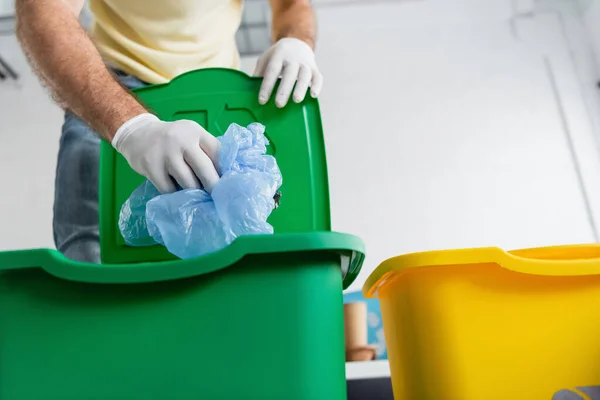 Ausgeschnittene Ansicht eines Mannes in Latexhandschuhen, der zu Hause Plastiktüten in Mülleimer steckt — Stockfoto