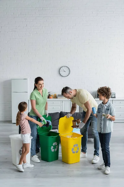 Весела родина сортує сміття в банках з емблемою переробки вдома. — стокове фото