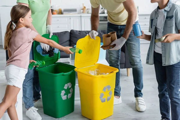 Enfants tenant des ordures près des parents dans des gants en latex et des canettes avec panneau de recyclage — Photo de stock