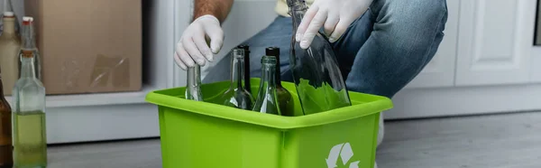 Vista recortada del hombre en guantes de látex sosteniendo botella cerca de la caja con cartel de reciclaje, pancarta — Stock Photo