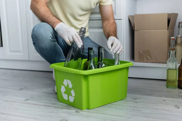 Vue recadrée de l'homme mettant bouteille dans la boîte avec panneau de recyclage dans la cuisine — Photo de stock