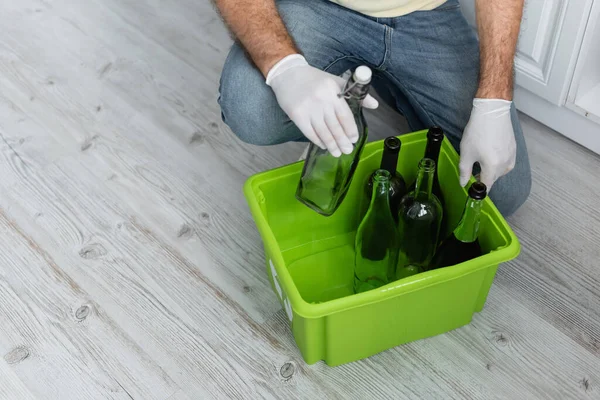 Vue recadrée de l'homme dans des gants en latex tenant boîte avec des bouteilles tout en triant les ordures — Photo de stock