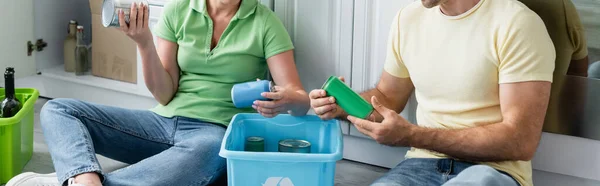 Обрезанный вид пары, держащей жестяные банки возле коробок во время сортировки мусора на кухне, баннер — стоковое фото