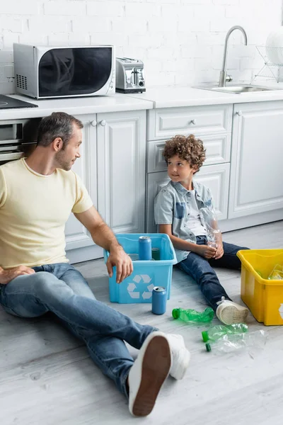 Ragazzo sorridente che guarda il padre vicino alle scatole con spazzatura in cucina — Foto stock