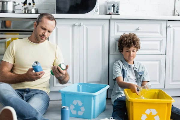 Hombre e hijo clasificando basura en cajas con cartel de reciclaje en la cocina - foto de stock