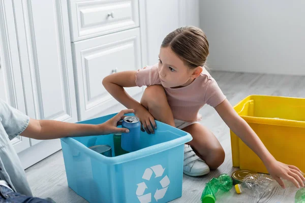 Chica sentada cerca de su hermano, cajas con basura y reciclar signo en la cocina - foto de stock
