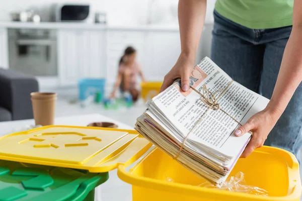 Cropped view of woman holding newspapers near trash can with recycle sing in kitchen — Stock Photo