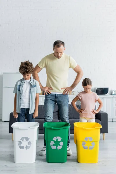 Père et les enfants regardant poubelles avec panneau de recyclage dans la cuisine — Photo de stock