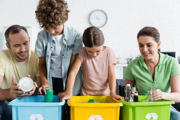 Família com crianças classificando lixo em caixas com sinal de reciclagem em casa — Fotografia de Stock