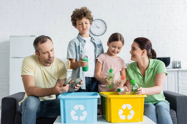 Lächelnde Familie sortiert gemeinsam Müll in Kisten mit Recycling-Symbol — Stockfoto