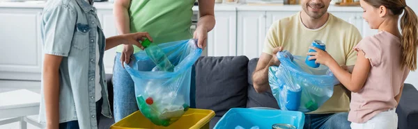 Crianças colocando lixo em sacos de lixo perto dos pais na cozinha, banner — Fotografia de Stock