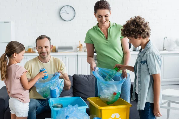 Enfants mettant des ordures dans des sacs près des parents dans la cuisine — Photo de stock