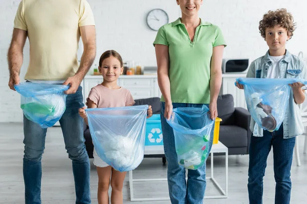 Smiling family holding trash bags in kitchen — Stock Photo