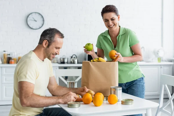 Mann hält Essen neben fröhlicher Frau und Papiertüte in Küche — Stockfoto