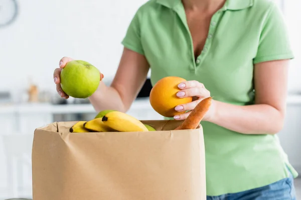 Обрезанный вид женщины, держащей свежие фрукты возле бумажного пакета — стоковое фото